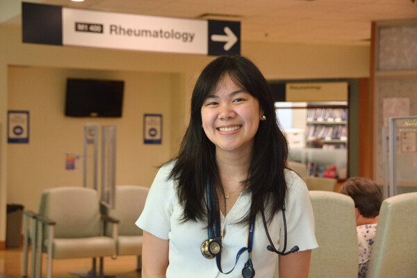 Person smiling in a clinical setting with seating in the background.