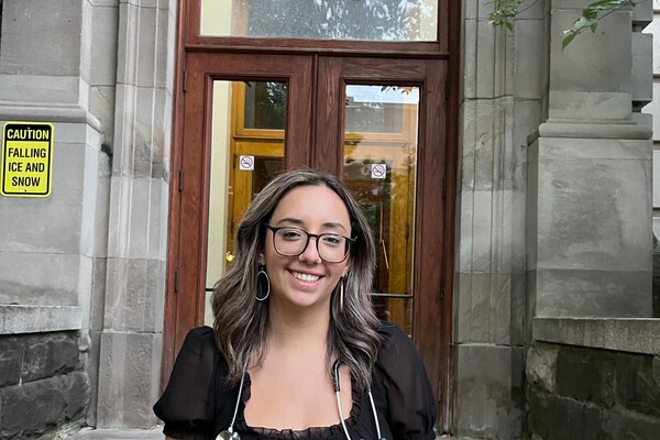 Smiling woman wearing glasses standing in front of a building with stethoscope around her neck.