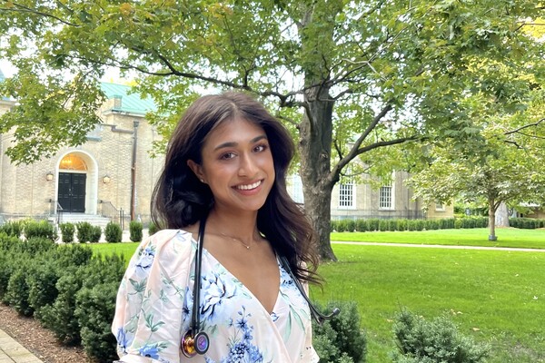 Smiling person in floral dress, with stethoscope on their shoulder with trees in the background